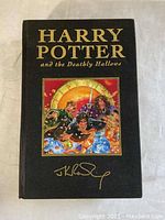 Front cover of hardcover book showing black cloth cover with gold foil 'Harry Potter and the Deathly Hallows' title, color illustration of characters, and gold J.K. Rowling signature.