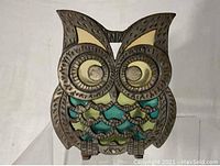 Front view of the owl napkin holder showing metal embossing details and colored stained glass style inserts.