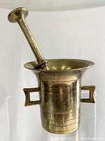 Front view showing the bronze mortar with its flared rim, two handles and pestle resting inside.