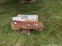 Partly assembled wooden yacht model hull on bespoke wooden cradle stand with wooden crate and original box contents in background.