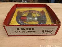 Vintage O.K. Cub .049 Class 1/2A marine engine in original red box with yellow backing, showing the engine and branding through a plastic cover.