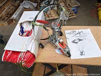 Top view of Sky Surfer RC paraplane showing parachute packed in box, paraplane frame with red propeller and pilot figurine, including instruction manual on table.