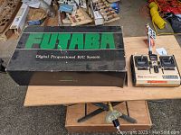 Photo of the Futaba controller and original box on a wooden table, showing the controller with two joysticks and switches and the box with 'FUTABA Digital Proportional R/C System' text.