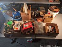 Overall view of eight cardboard boxes and containers filled with model airplane engines, boxes and parts on tabletop