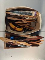Photo of two boxes filled with mostly wooden model airplane propellers of various sizes and shapes, some with tags.