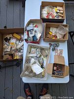 Six boxes and bins on a folding table containing a jumble of small packaged and loose engine parts