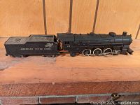 Side view of entire train set showing locomotive and tender connected, displayed on wooden surface with wood panel background
