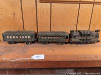 Three Lionel O gauge train models lined up on a wooden shelf, including a locomotive and two passenger cars, showing overall condition and size.