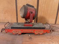 Front angled view of the vintage tin spotlight railcar toy showing the large mounted spotlight and flatbed base with printed red details.