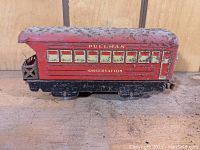 Side view of vintage red and black tin observation caboose with visible lettering and weathering.