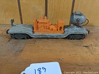 Gray flatcar with centrally mounted orange generator and large searchlight at one end, showing side details and Lionel Lines 6520 marking.