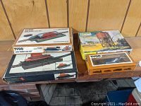 Four HO gauge TYCO train items in original boxes displayed on a wooden ledge, including an ore dump car set, a water tower, a horse car locomotive, and an additional accessory.