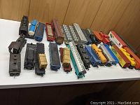 Full view of the lot of HO gauge model trains including locomotive engines and multiple types of freight cars arranged on a white surface.