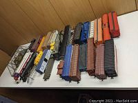 Wide shot of assorted HO scale freight cars arranged on white tabletop against wood-paneled background