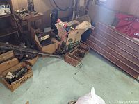 Wide view showing several cardboard boxes containing various train track pieces, transformers and other accessories on a basement floor