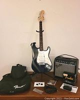 Guitar on stand with gig bag, two amplifiers, tuner, picks, cable and spare parts on table