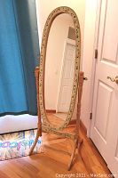 Full view of the floor mirror standing upright showing the oval glass and floral painted frame.