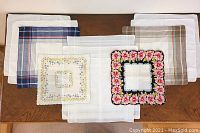 Collection of eleven men's and women's handkerchiefs laid out on wooden surface, showing different patterns including plaids and floral prints.