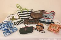 Twelve assorted bags, wallets, and makeup bags of various colors and styles including striped, floral, leopard print, and patterned designs, laid out for viewing.