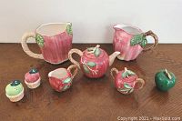Full set showing all 8 items including teapot, sugar bowl, creamer, two pitchers, salt and pepper shakers, and paperweight on a wood surface.