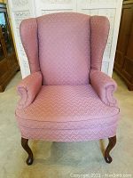 Front view of the vintage mauve/pink chevron textured wingback armchair with padded armrests and curved wooden legs.