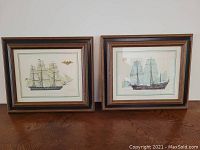 Two framed ship prints side by side on a wood surface