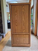 Closed view of the tall wood grain rolling storage cabinet with two vertical doors and a bottom compartment, showing overall exterior condition and wood pattern.