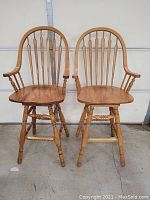 Front view of two oak bar stools with armrests and spindle backrests showing wood grain and condition.