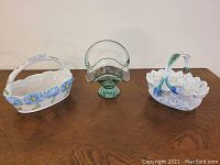 Front view showing all three baskets on wooden surface: green glass basket center, blue floral ceramic basket left, larger Vietri ceramic basket right