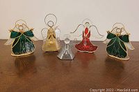Five metal and stained glass angel tealight holders in various colors including green, red, gold, and silver arranged in a row on a wooden table