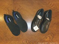 Two pairs of men's shoes displayed on wooden surface. Black leather Hush Puppies with slip-on moccasin style and black suede King Size shoes with Velcro strap.