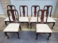 Photo showing the set of six vintage dining chairs arranged in two rows, wood frames with curved backrest design, cream colored upholstery on seats.