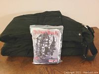 Folded black ski bibs with a sealed package of Helmet Heads helmet cover on top on a wooden table