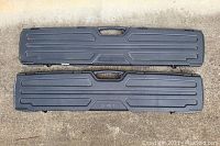 Top-down photo showing two black hard plastic hunting gun cases side by side on concrete. One has RedHead and the other Plano Gun Guard branding.
