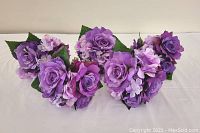 Five small purple artificial flower bouquets arranged on a white surface showing variety and size