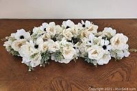 Eight small white artificial flower bouquets arranged on a wooden surface.