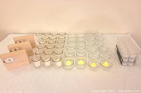 41 clear glass candleholders arranged in rows with seen three dozen white votive candles and 30 flameless electronic tealights, some lit inside candleholders.