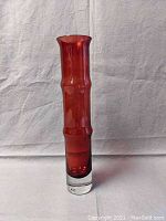 Full front view of the tall red glass vase with ribbed pattern and clear thick base.
