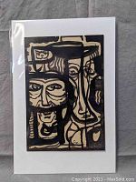 Ink on paper artwork showing abstract faces with strong black lines. Protective plastic sleeve is visible.