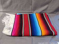 Folded vibrant South American wool blanket showing colorful horizontal stripes with white fringed edges.