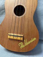 Close up of body showing natural wood grain finish and 'The Hawaiian' lettering in yellow.