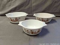 Front-side view showing three nested white glass Pyrex bowls with brown floral pattern on the sides and handles on both ends.
