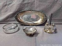 Photo showing entire lot: silver plated tray, glass dish, small basket, and condiment set on a gray fabric background.