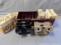 Front view of the two stereo viewers, black and beige, with some slide reels in a holder.