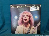 Front cover of 'Frampton Comes Alive!' double vinyl album showing Peter Frampton with guitar, blue background, and text indicating 2 records included.