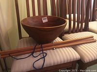 Side angle view showing the teak bowl resting on the wooden stand across two striped chairs.