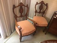 Pair of antique parlour chairs, one with arms and one without, both upholstered in pink fabric with carved wooden frames.