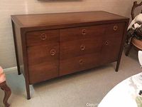 Front view of mid century modern Drexel buffet showing three drawers and two cabinet doors with round inset wood and black knob handles.
