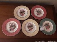 Five Wedgwood Queen's Ware luncheon plates with varied colored borders and floral center illustrations, showing the designs and arrangement of the lot.