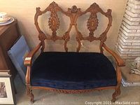 Front view of the antique wooden carved settee with blue upholstered seat showing overall condition and design details.
